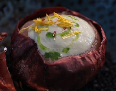Gourmet onion soup served in a roasted onion skin with creamy foam and edible yellow petals.
