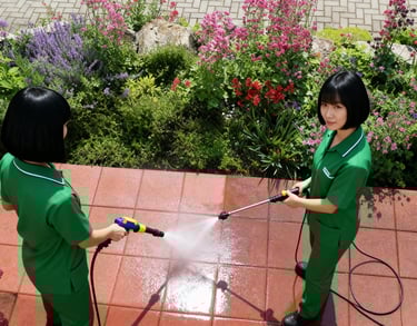 two women in a green uniforms pressure washing a patio