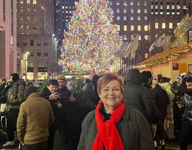 Photo of Debbie in front of a giant, multicolored Christmas tree in a crowded urban plaza.