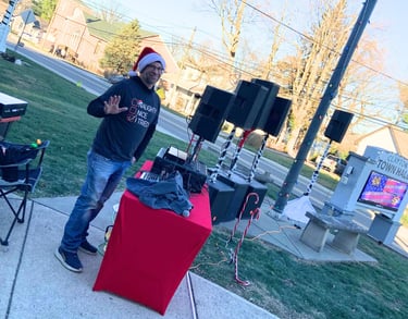 guy in holiday shirt and hat with music equipment waving at the camera