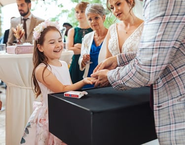 Enfant qui sourit devant un magicien lui faisant un tour de magie durant un mariage.