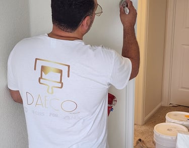 A professional painter using a brush to apply white Benjamin Moore paint to an interior wall corner.