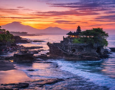 This image shows a dramatic sunset view of Tanah Lot temple in Bali with ocean waves, glowing sky, a