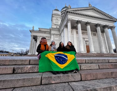 Quatro fundadoras do BiF sentadas na escadaria da Catedral de Helsinki, com a bandeira do Brasil cobrindo as pernas