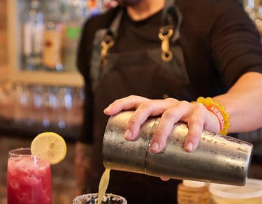 Bartender wearing a black apron, pouring a cocktail from a shaker into a glass with a salted rim