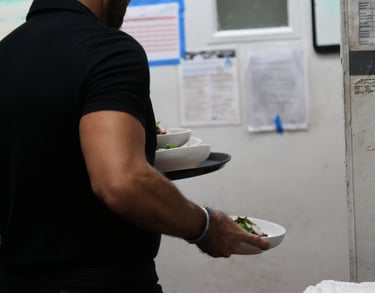 Close-up of a server dressed in black, carrying several plates with both hands.