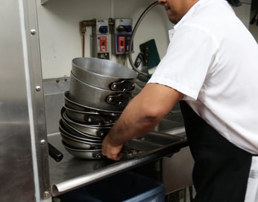 Close-up of a person stacking clean metal pots on a kitchen sink in a professional kitchen setting.