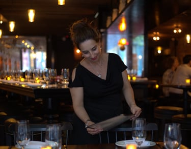 Smiling woman dressed in black, holding a menu in a restaurant setting