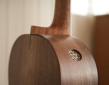 Close-up of a handcrafted acoustic guitar with a walnut body and a unique side sound port.