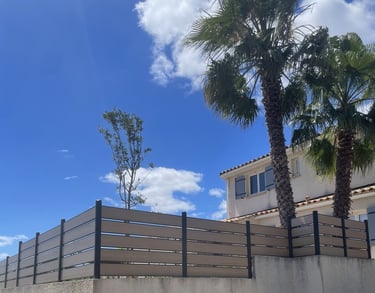 Clôture composite gris clair installée dans un jardin avec palmiers