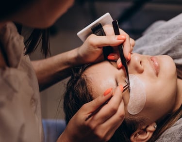 Professional lash artist applying individual eyelash extensions using precision tweezers in a beauty salon.