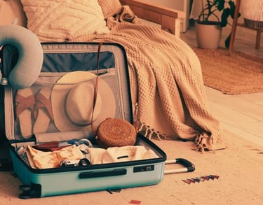 Open suitcase packed with travel essentials like a sun hat, neck pillow, and clothes on a cozy rug.