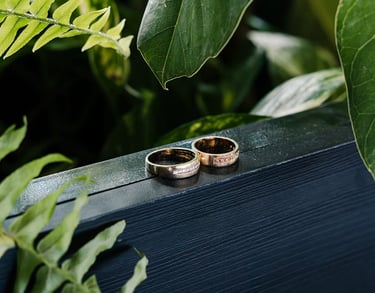 Fotografía premium de detalle de anillos de bodas reodeados de plantas en un fondo de madera azul en Quito