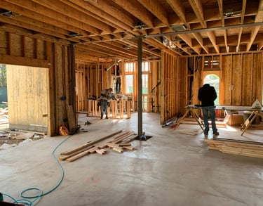 Construction workers framing a new house interior with wooden studs and floor joists on a concrete slab.