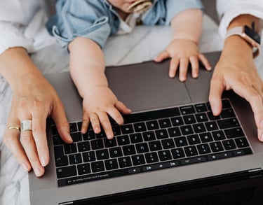 a mother typing on a laptop with a baby's hands also on the keyboard