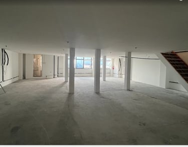 Empty commercial office space with white walls, concrete floors, support pillars, and a staircase.