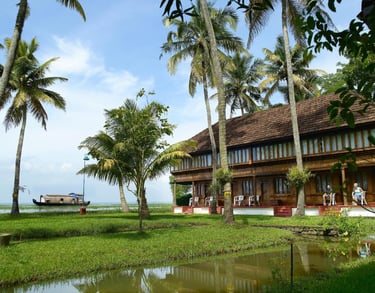 Traditional Kerala house surrounded by palm trees and lush greenery, overlooking tranquil backwaters.
