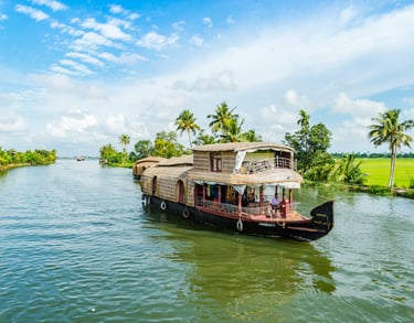 Houseboat cruising through Kerala's backwaters, surrounded by lush palm trees and vibrant greenery under a blue sky.