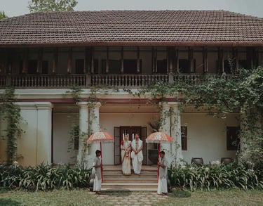 Heritage stay in Kerala featuring a couple in traditional attire, flanked by attendants holding umbrellas.