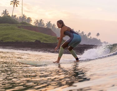 Girl surfing on a wave in Varkala, Kerala, with palm trees and cliffs in the background during sunrise.