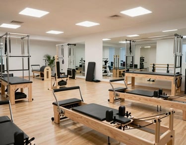 Gym and rehabilitation area of the clinic. Pilates reformers and functional training gear, bright open space with wooden floors and high ceilings.