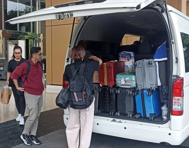 Satu orang pria dua orang wanita sedang menurunkan bagasi dari Hiace.