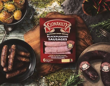 Clonakilty black pudding pork sausages on a wooden board with cooked potatoes and Irish black pudding.