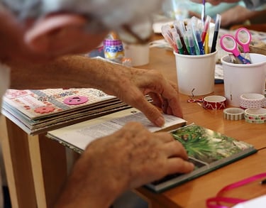 Un adulto mayor, haciendo una manualidad de un libro en una mesa de madera.
