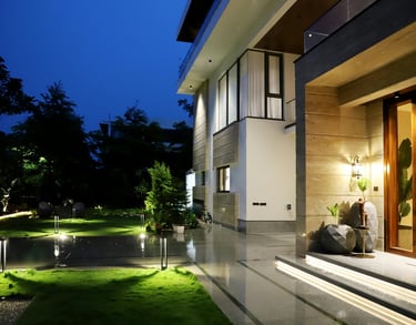 Modern luxury house exterior at night with glowing landscape lighting and manicured garden.