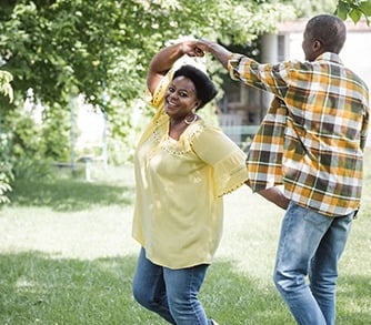 A joyful couple dancing and twirling in a sunlit green garden during summertime