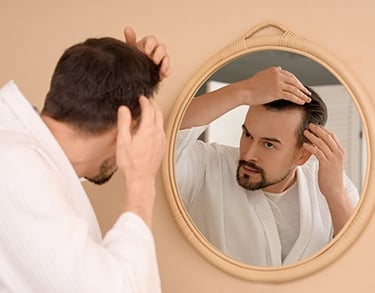 man-checking-hair-loss-thinning-hair-mirror-scalp-concern