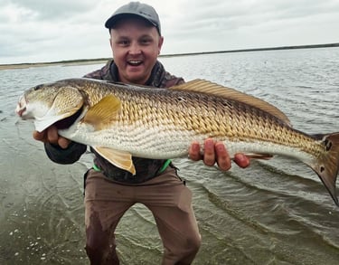 Will Bonniville holding a redfish on the shoreline near the ocean