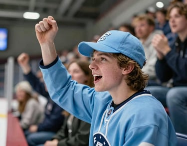 A shot of a young fan wearing a sky blue team cap, cheering in the stands of a collegiate rink. The background shows a blurry crowd and professional sports lighting. North American / US Southern context.