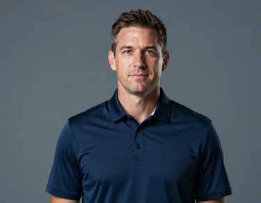 Studio portrait of a sports professional wearing a dark navy blue polo shirt with a subtle collar detail. Professional lighting, neutral gray-blue backdrop, North American / US Southern athletic director persona.