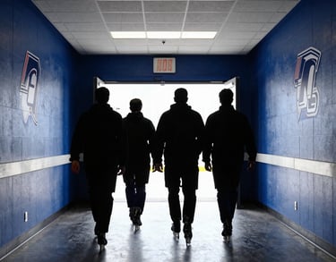 A team walking down a hallway towards the rink entrance, silhouettes against the bright light of the arena. The walls are royal blue with athletic decals. North American / US Southern university sports facility.