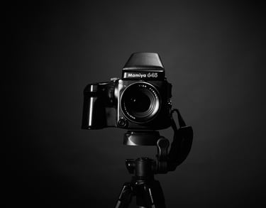 A black and white studio shot of a Mamiya 645 medium format film camera mounted on a professional tripod.