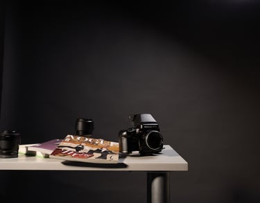 Mamiya 645 film camera and lenses on a desk next to fashion magazines in a studio setting.