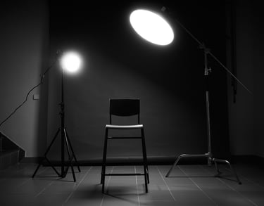 Professional photography studio setup with a chair under bright studio lights and black background.