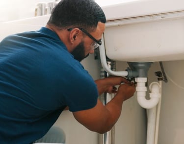 Plombier pro en lunettes fixant le siphon et le drain d'un évier de cuisine.