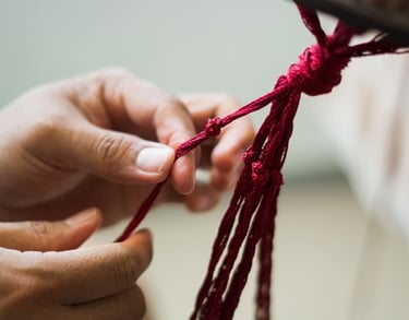 Manos atando nudos intrincados en un cordón rojo para un proyecto artesanal de macramé hecho a mano