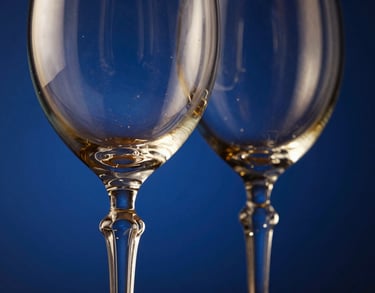 Close-up of elegant hand-blown crystal wine glass rims catching hard dramatic side-lighting, deep blue background, 35mm