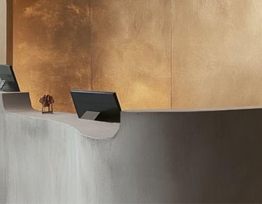 A modern reception desk with computer monitors, set against a microcement wall
