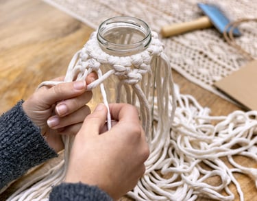Manos tejiendo macramé con cordón blanco.