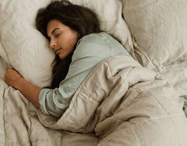 Uma mulher dormindo confortavelmente em uma cama com lençóis macios de linho e um cobertor bege.