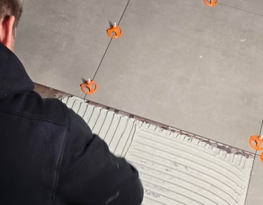 Professional contractor installing large format floor tiles with orange leveling spacers and thinset mortar.