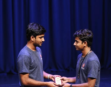 A high-angle shot of a South Asian student athlete receiving an award on a stage. Royal blue curtains in the background and soft stage lighting.
