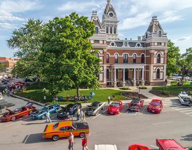 Classic muscle cars gathered at a summer car show in front of a historic  brick pontiac IL