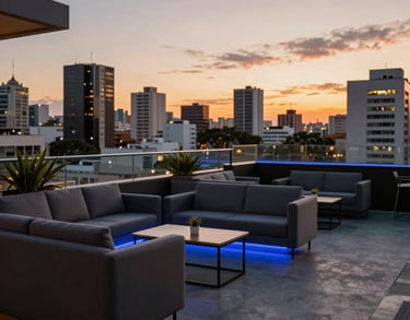 An outdoor corporate lounge at sunset in a South American city, featuring comfortable modern seating, ambient blue lighting, and a view of urban architecture.