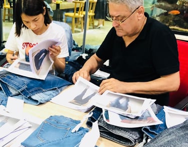 Fashion designers reviewing denim samples and product photos at a workstation for apparel manufacturing.