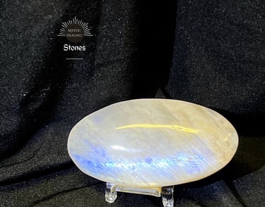 Polished oval moonstone palm stone with blue flash on a stand against black fabric.